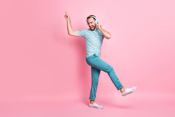 Взгляд на размер тела в полный рост привлекательного веселого парня, слушающего бас-гитару, танцующего, веселясь на фоне розового цвета - Фото, изображение