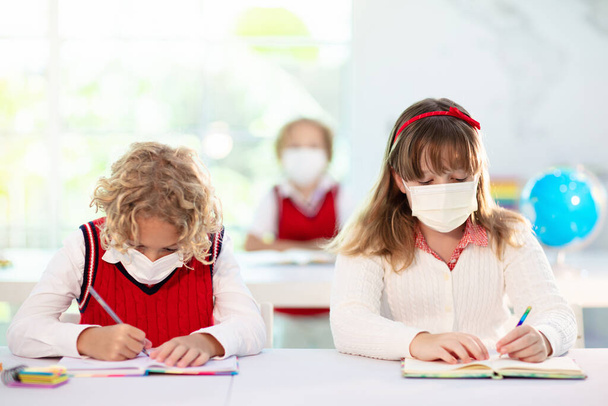 Kids in face mask in school class. Child back to school after coronavirus lockdown. Primary child in covid-19 pandemic. Safety and virus spread prevention. Student in surgical mask. Social distancing. - Foto, Imagen