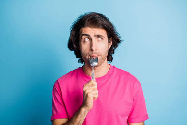 Portrait of attractive bewildered guy licking spoon counting calories healthy menu regime isolated over bright blue color background - 写真・画像