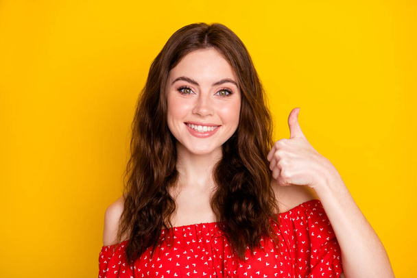 Photo portrait of curly happy girl smiling in printed dress showing thumb-up sign gesture isolated vivid yellow color background - 写真・画像