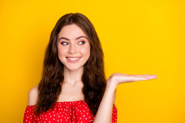 Photo portrait of nice girl in red shirt curious keeping blank space on palm isolated vibrant yellow color background - Photo, Image