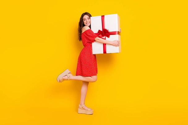 Full size profile portrait of positive charming lady hands hold large giftbox isolated on yellow color background - Foto, afbeelding