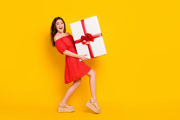 Full body profile portrait of astonished pretty lady hands hold large heavy giftbox isolated on yellow color background - Fotó, kép