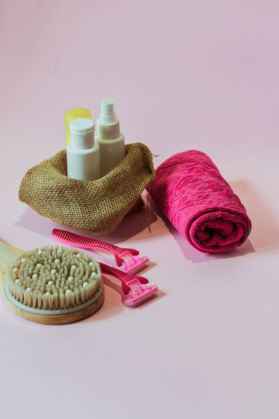 Bottiglie bianche di prodotti per la cura del corpo, un banco massaggi in legno, un asciugamano rosa, rasoi rosa stare su uno sfondo rosa. - Foto, immagini