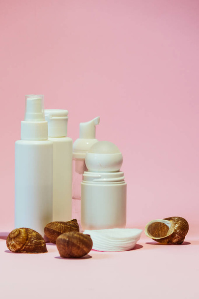 Les produits essentiels d'hygiène et de soin du corps dans des bouteilles blanches reposent sur un fond rose à côté des coquillages. - Photo, image