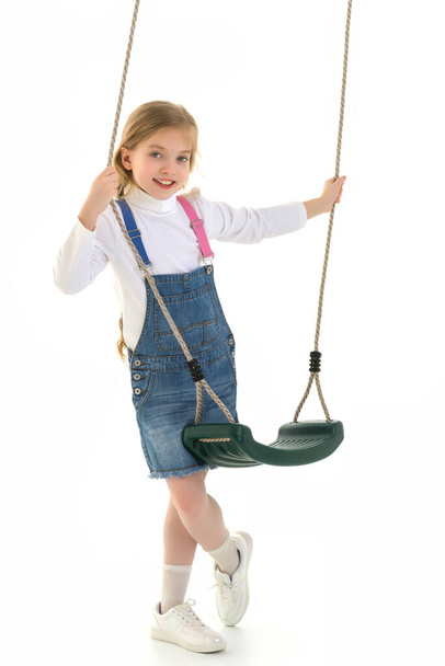 Cute little girl is standing near the swing. - Фото, изображение