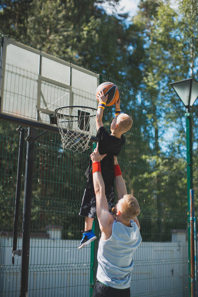 Happy family playing basketball. Young sportive father with son in hands. Kid boy throwing ball in basketball hoop - Foto, afbeelding