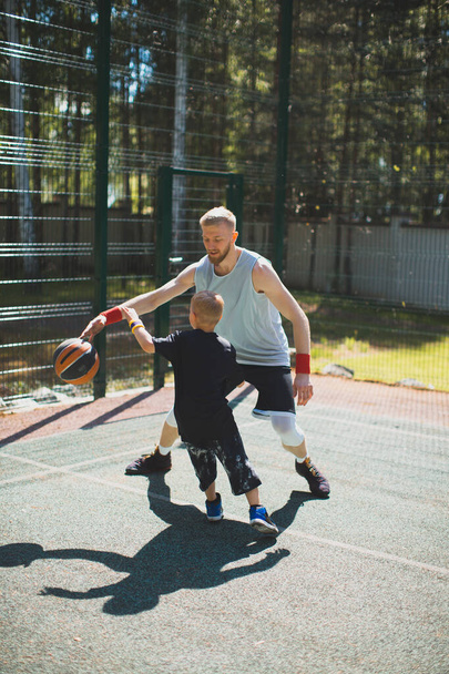 Professional american basketball player instructor train little sports boy outdoor on basketball court - Фото, изображение