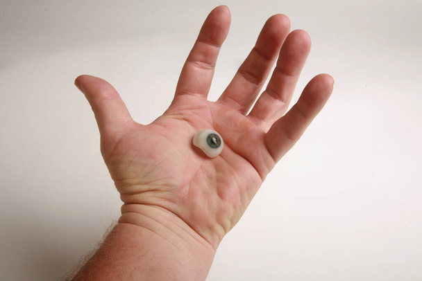 человеческая рука держит настоящий стеклянный глаз. антикварный протез глаза. стеклянный глаз. фальшивый глаз. человеческий глаз. медицинский стеклянный глаз. античный человеческий стеклянный глаз. - Фото, изображение
