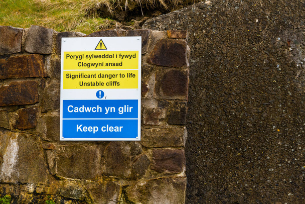 sign in welsh and English Significant danger to life unstable cliffs at Nefyn, Llyn Peninsula, Wales, UK. This happened in April 2021, this image taken in May 2021, landscape, copyspace to right. - Photo, Image