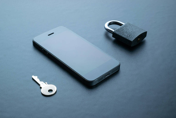Business security protection. Modern space grey mobile phone with padlock, key on dark background. Smartphone fraud, online scam and cyber security threat - Fotografie, Obrázek