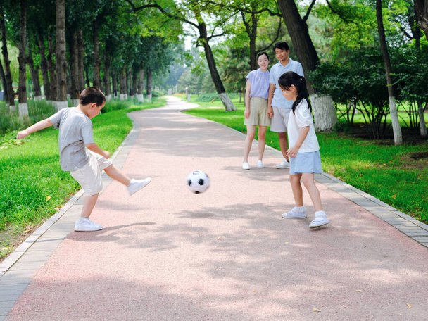 Happy family of four playing football in the park - Фото, изображение