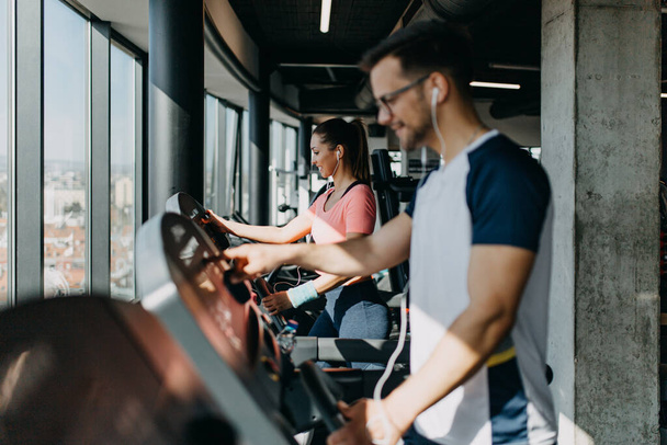 Young fit man and woman running on treadmill in modern fitness gym. - Foto, imagen