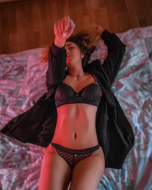 Pretty fitness sexy girl laying on bed . Glamour legs and seductive silhouette , sensual portrait standing under neon trendy lights . Erotic figure of beautiful woman in elegant lingerie - Foto, immagini