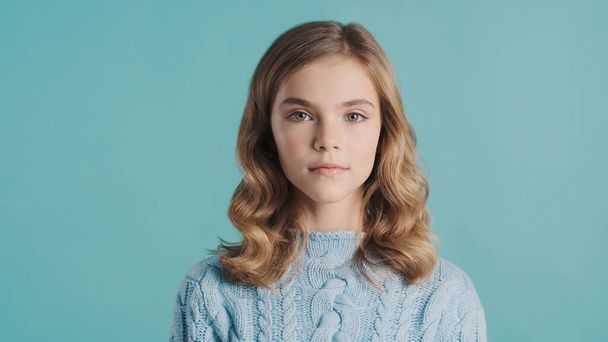 Pretty blond haired teenage girl dressed in cozy sweater looking confident on camera over blue background - Fotó, kép