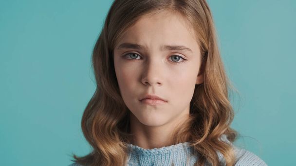 Portrait of upset blond teenage girl looking offended and sad isolated on blue background. Face expression - Foto, Imagen