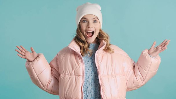 Emotional blond teenager girl dressed in pink down jacket and hat happy to meet best friend over colorful background. Cheerful teen girl - Foto, Imagen