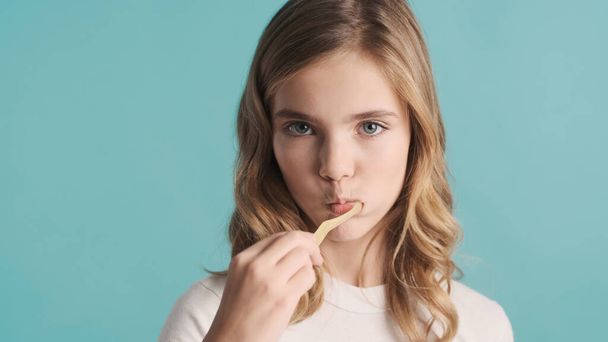 Portrét blond dospívající dívka čištění zubů na kameře izolované na modrém pozadí - Fotografie, Obrázek