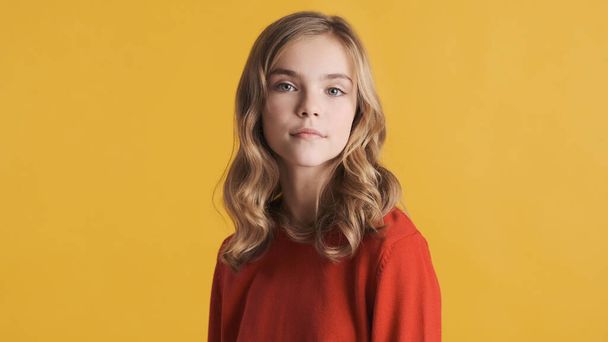 Atraktivní blond vlnité vlasy dospívající dívka v červeném svetru vypadá sebevědomě pózovat na kameře izolované na žlutém pozadí - Fotografie, Obrázek