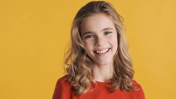 Veselý blond dospívající dívka hledá okouzlující úsměv na kameře izolované na žlutém pozadí - Fotografie, Obrázek