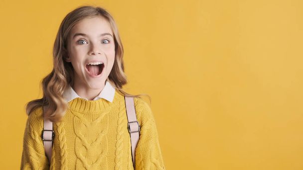 Cheerful blond teenage student girl looking excited standing near copy space for your advertisement or promotional content isolated on yellow background - Foto, Imagen