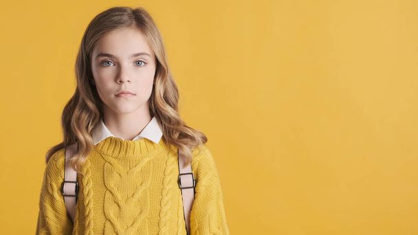 Krásná blond teenager studentská dívka hledá jistotu stojící v blízkosti kopírovat prostor pro vaši reklamu nebo propagační obsah přes žluté pozadí - Fotografie, Obrázek