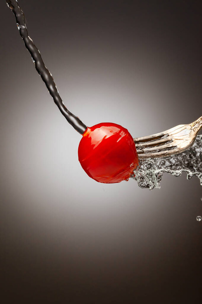 small cherry tomatoes on a silver fork are poured with water. Splashes of water. Gradient background. Vertical frame. Place under the text - Photo, Image