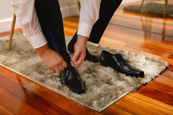 Homem calçando um sapato preto, amarrando o cadarço, vestindo calças azuis escuras, vestindo roupas de negócios - Foto, Imagem