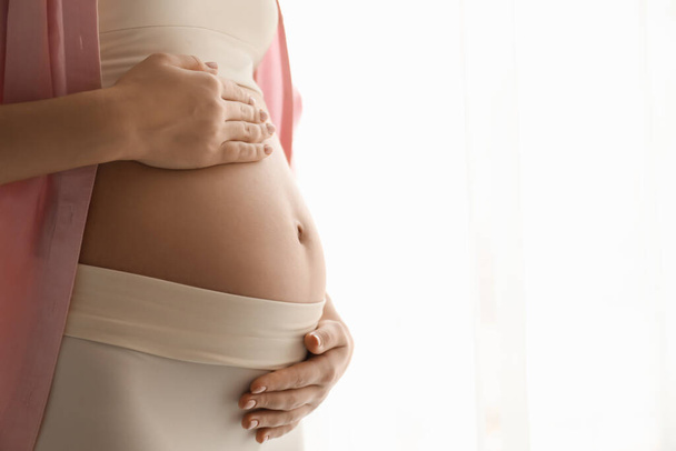 Pregnant young woman touching belly on light background, closeup. Space for text - Fotoğraf, Görsel