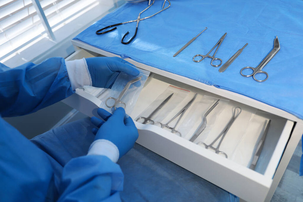Doctor putting Pott's scissors into drawer indoors, closeup. Table with different surgical instruments - Fotó, kép