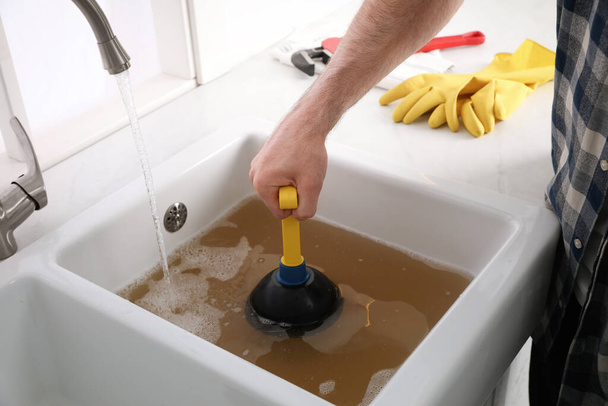 Man using plunger to unclog sink drain in kitchen, closeup - 写真・画像