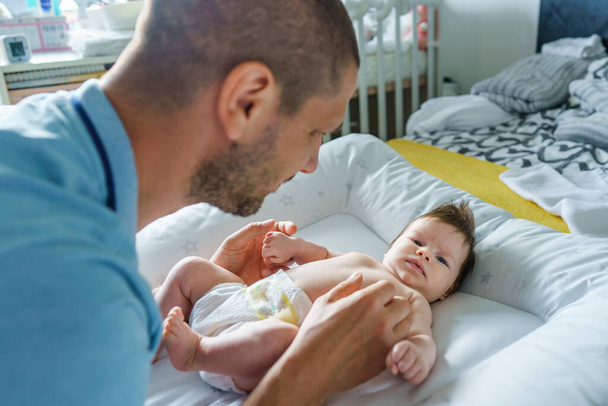 Kaukasischer Mann Vater kümmert sich um sein zwei Monate altes Baby Junge oder Mädchen auf dem Bett zu Hause Windeln und Kleidung wechseln - Vatertagselternschaft Konzept echte Menschen Familie - Foto, Bild