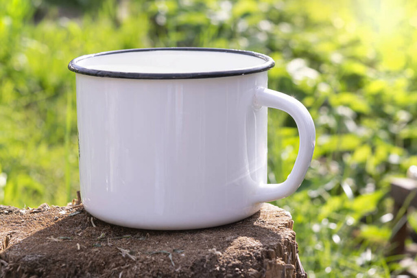 An old, cracked metal mug with a place for text on a wooden stump.A mug of water for a picnic, quenching your thirst on a hot day against the background of foliage. - Photo, image