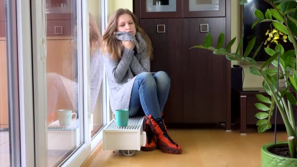 junge Frau erfror zu Hause auf Heizkörper im Wohnzimmer sitzend. 4K - Filmmaterial, Video