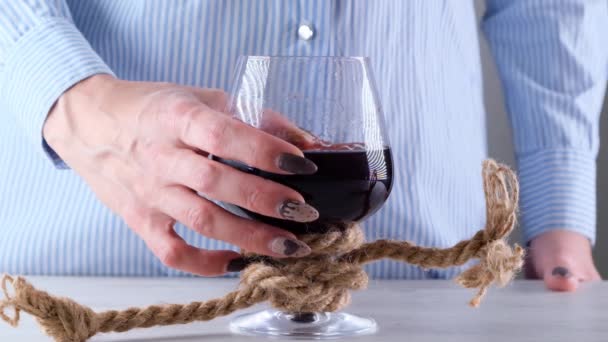 жіноча рука, що тримає келих для вина, пов'язана джутовою мотузкою. Поняття алкогольної залежності
. - Кадри, відео