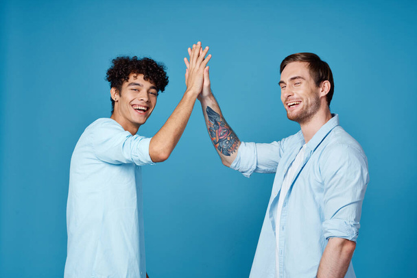 een man met een tatoeage schudt handen met een krullende man op een blauwe achtergrond vrienden communicatie - Foto, afbeelding