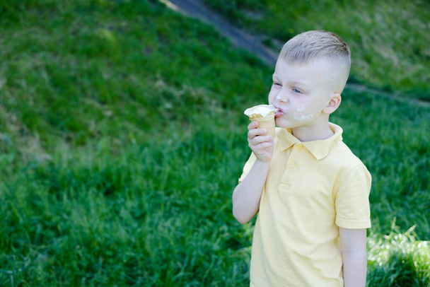 Boy eating ice cream with stains around his mouth. outdoors in the park. High quality photo - Zdjęcie, obraz