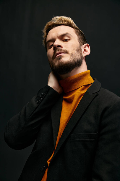 confiado joven rubio hombre en chaqueta naranja suéter sobre fondo oscuro levantó la cabeza hacia arriba vista recortada - Foto, Imagen