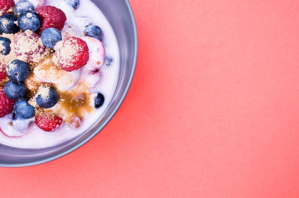 A top view of yogurt with raspberries, blueberries, and powder on a bowl isolated on red background - Фото, изображение