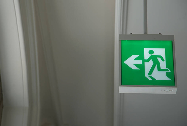 Un segnale verde di uscita di emergenza appeso a un soffitto interno                                - Foto, immagini