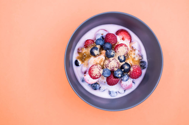 A top view of yogurt with raspberries, blueberries, and powder on bowl isolated on orange background - Foto, imagen
