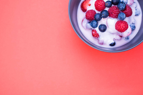 A top view of yogurt with fresh raspberries and blueberries on a bowl isolated on red background - Foto, afbeelding