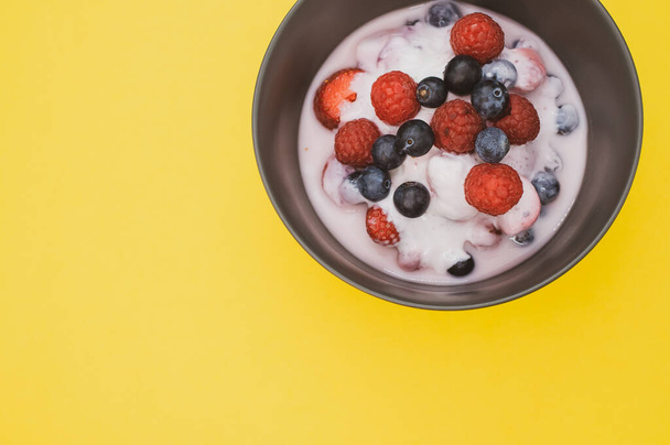 A top view of yogurt with fresh raspberries and blueberries on a bowl isolated on yellow background - Foto, immagini