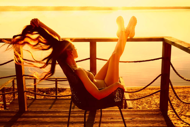 latin hispanic Girl with long hair sitting in a armchair lounge and sunbathing on the balcony on the background of the seascape view. - Fotó, kép