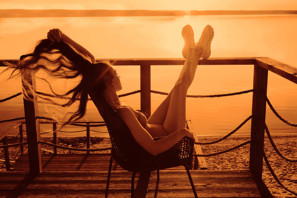 latin hispanic Girl with long hair sitting in a armchair lounge and sunbathing on the balcony on the background of the seascape view. - Valokuva, kuva