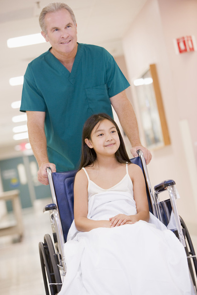 An Orderly Pushing A Little Girl In A Wheelchair Down A Hospital - 写真・画像