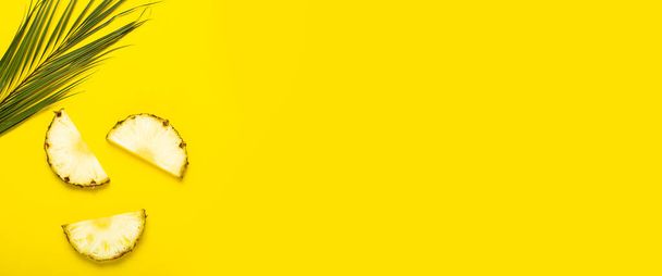 Rodajas de piña maduras, piña con follaje y una hoja de palma sobre un fondo amarillo. Vista superior, plano. - Foto, Imagen