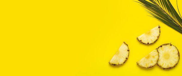 Érett ananászszeletek, ananász lombozattal és pálmalevél sárga háttérrel. Felülnézet, lapos fektetés. - Fotó, kép