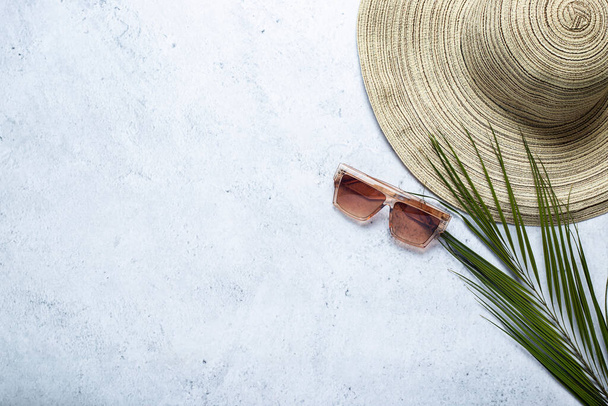 Women's hat, sunglasses and a leaf of a palm tree on a concrete background. Top view, flat lay. - Foto, Bild