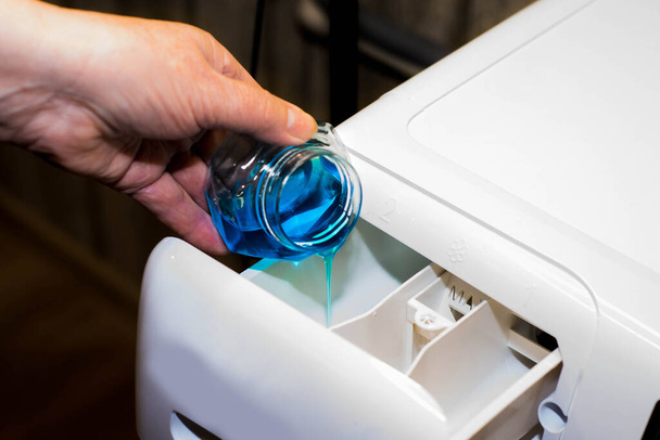 Çamaşır makinesine mavi renkli sıvı çamaşır tozu dökülüyor. - Fotoğraf, Görsel